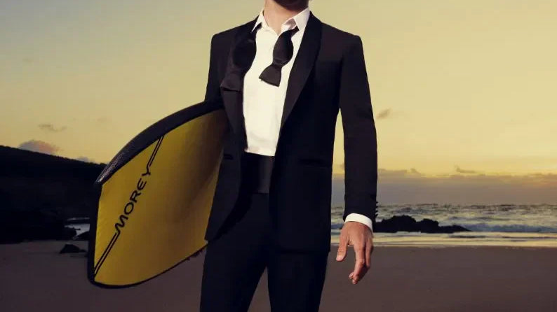 Man in suit holding yellow bodyboard on beach at sunset