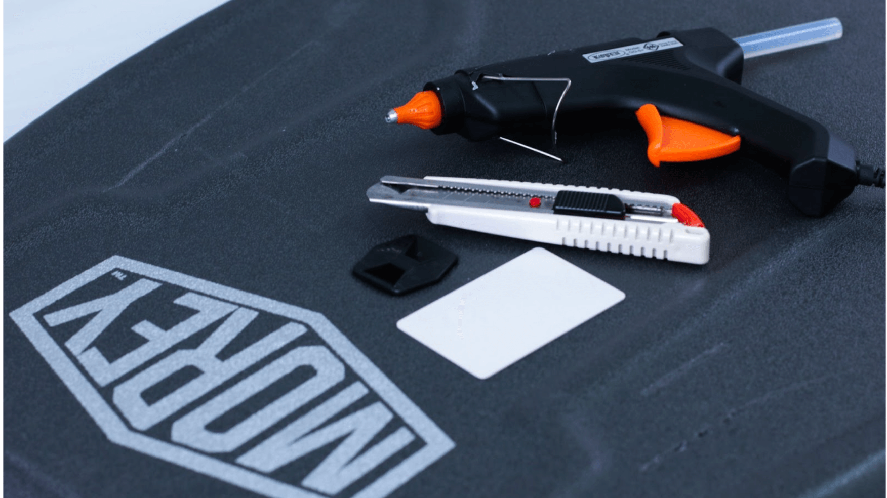 Hot glue gun and utility knife on black Morey board with card and tool.