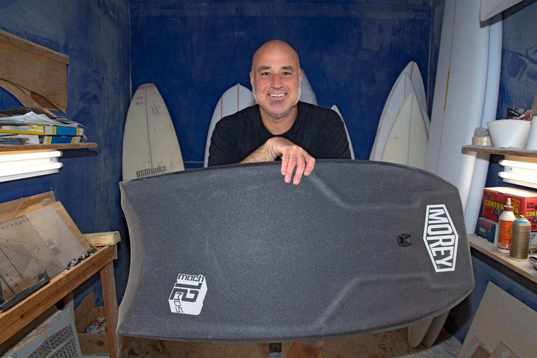 Man holding Morey Mach 25 bodyboard in surfboard shaping workshop