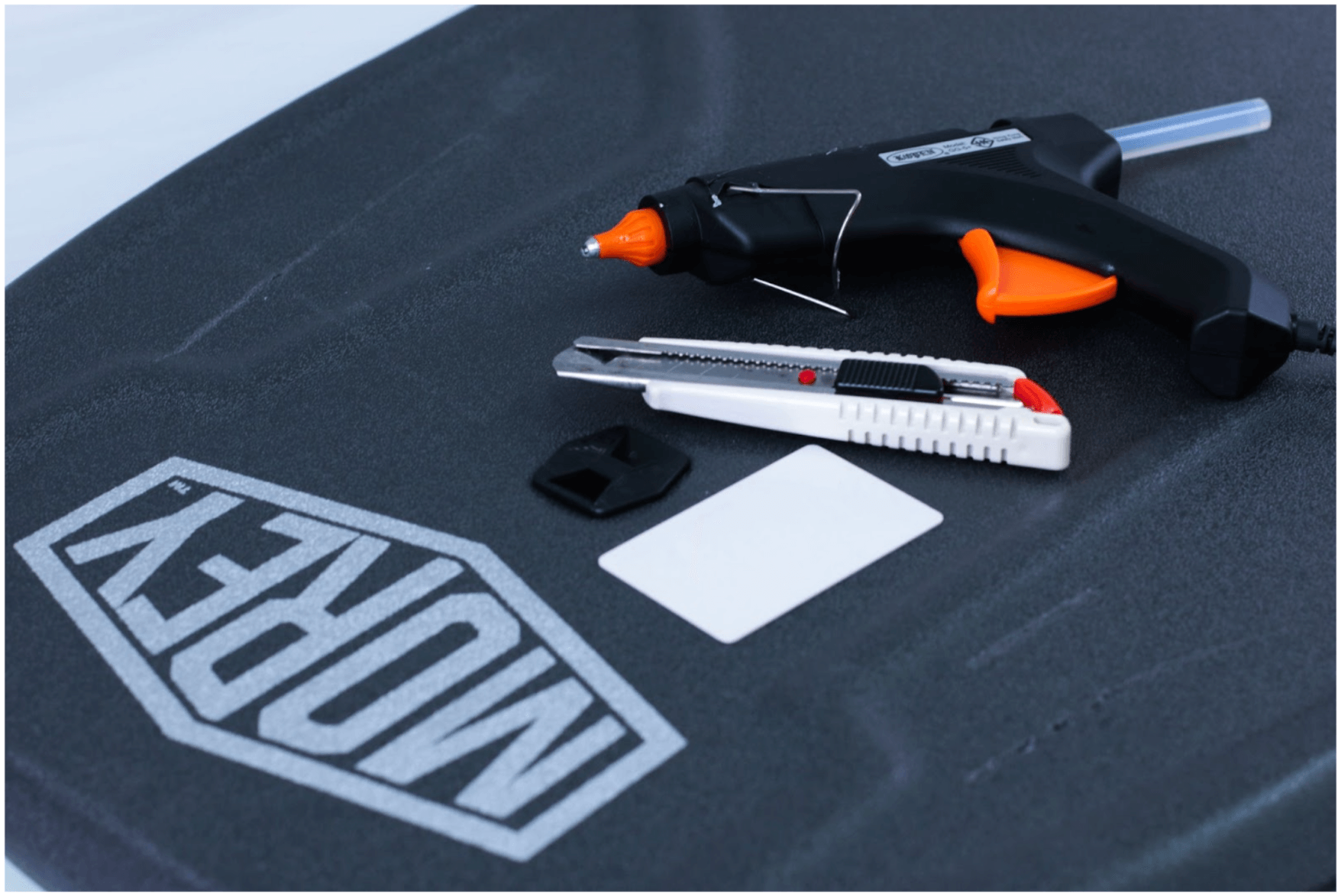 Black and orange hot glue gun and white utility knife on black surface with IMPREY logo