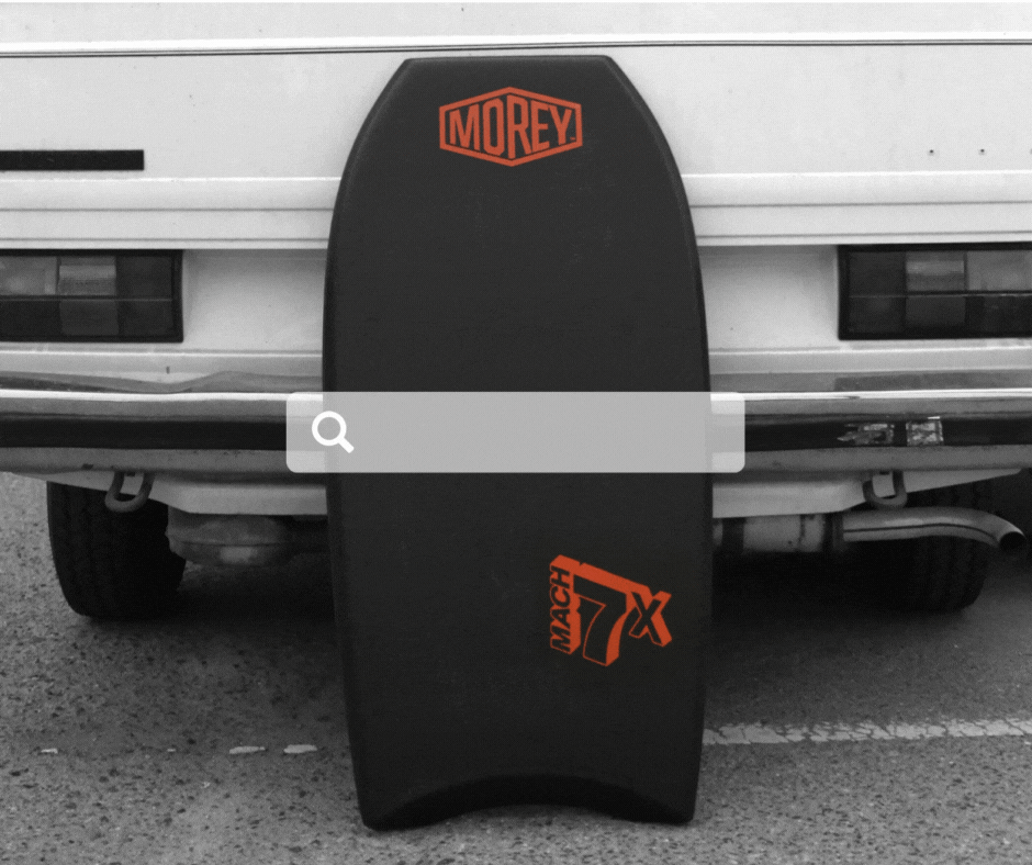 Black bodyboard with orange logo and Mach 7X design leaning against a car bumper
