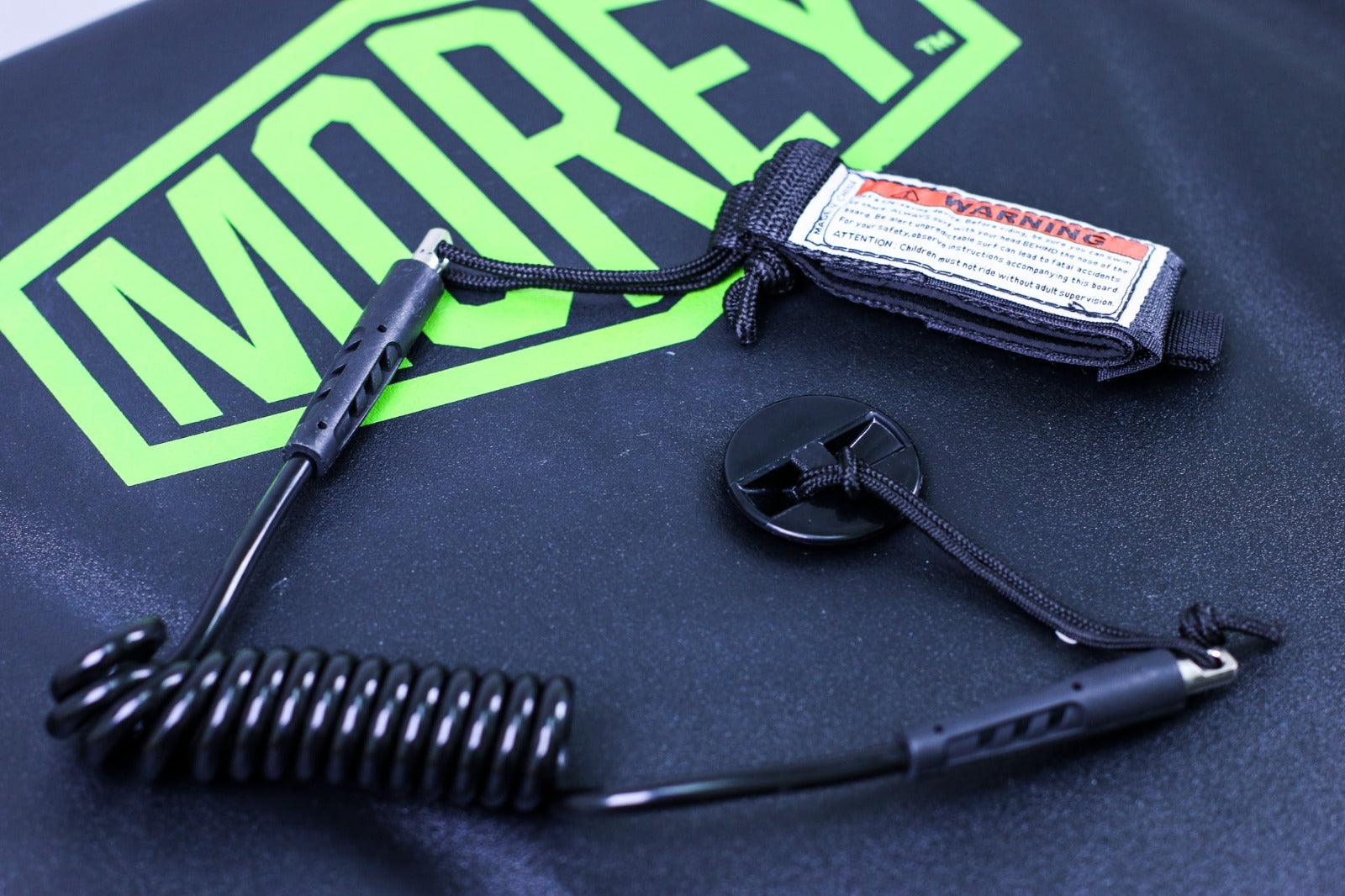 Black coiled safety leash with warning label on green MOREY logo background