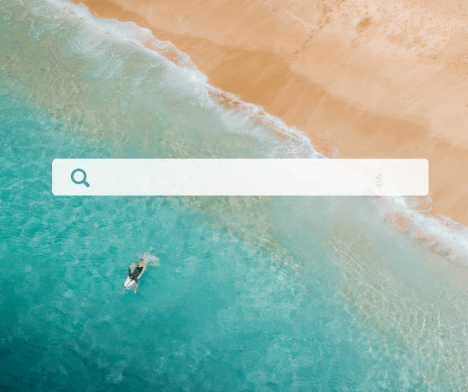 Aerial view of a surfer paddling on a surfboard in clear turquoise ocean near a sandy beach with gentle waves
